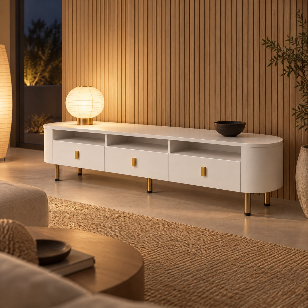 Meuble TV blanc arrondi 3 tiroirs pieds dorés 174 cm, dans un salon le soir